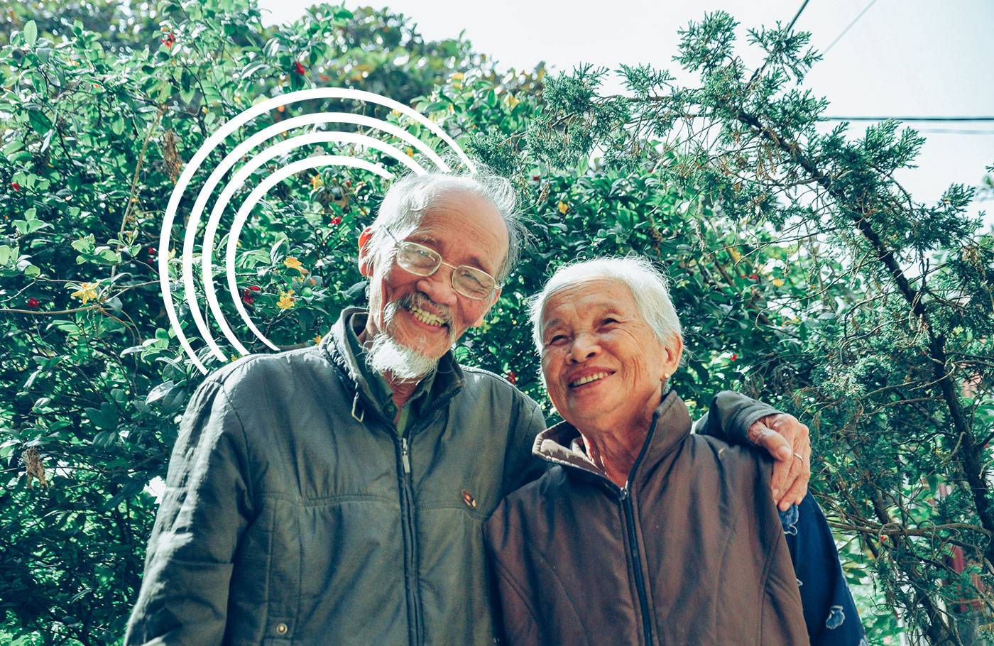 An elderly Asian couple standing outdoors and smiling