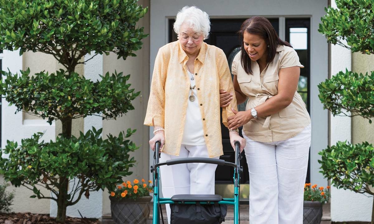 Caregiver helping elderly woman with walker, exemplifying caregiver support and resources
