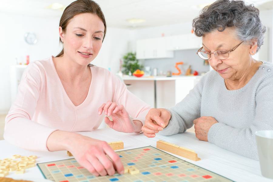 An adult woman and an elderly woman play a board game in their kitchen