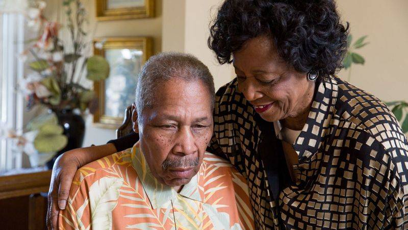 Elderly African American couple, woman is smiling and man looks solemn