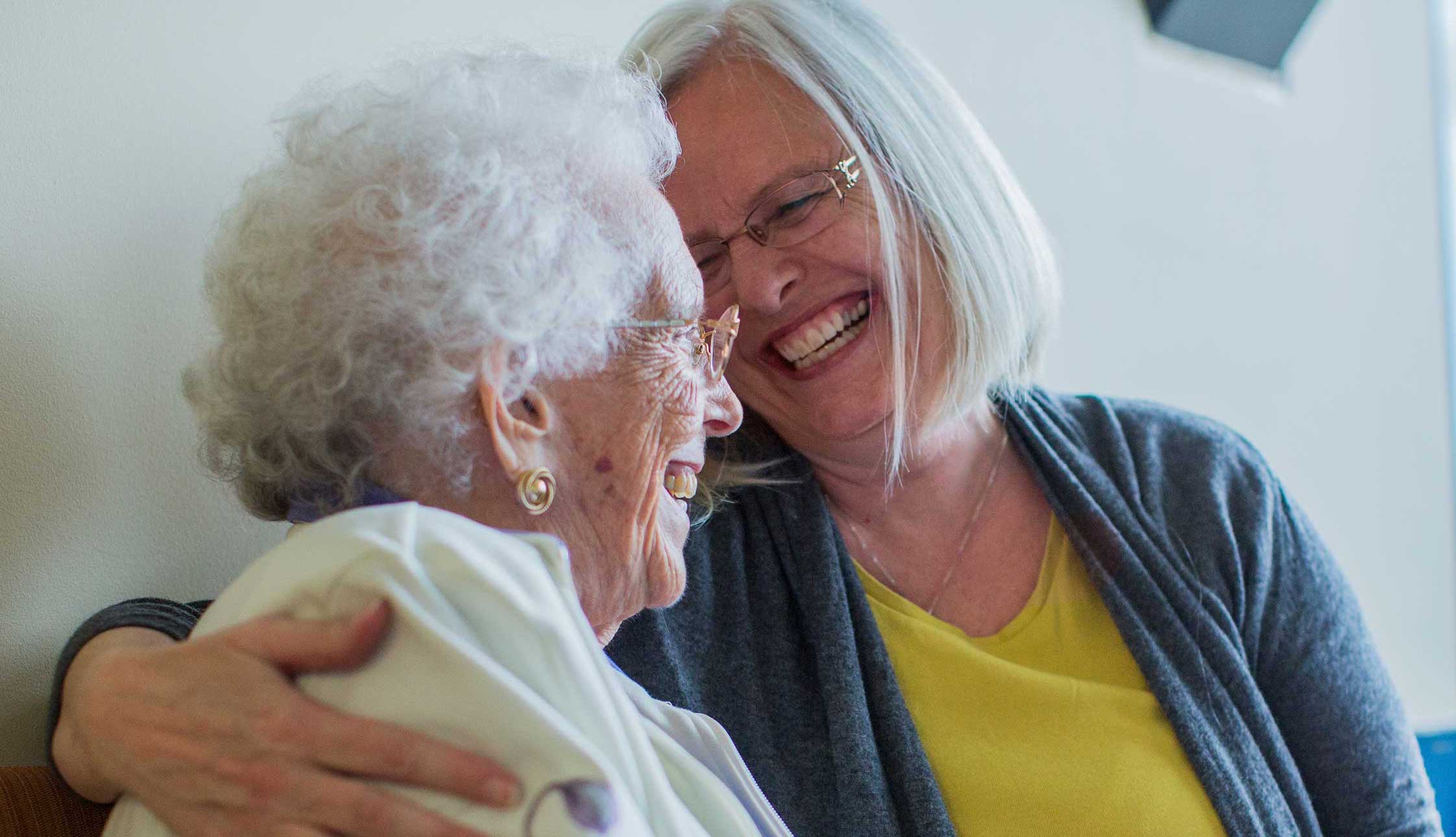 Elderly mother and adult Daughter embrace on couch