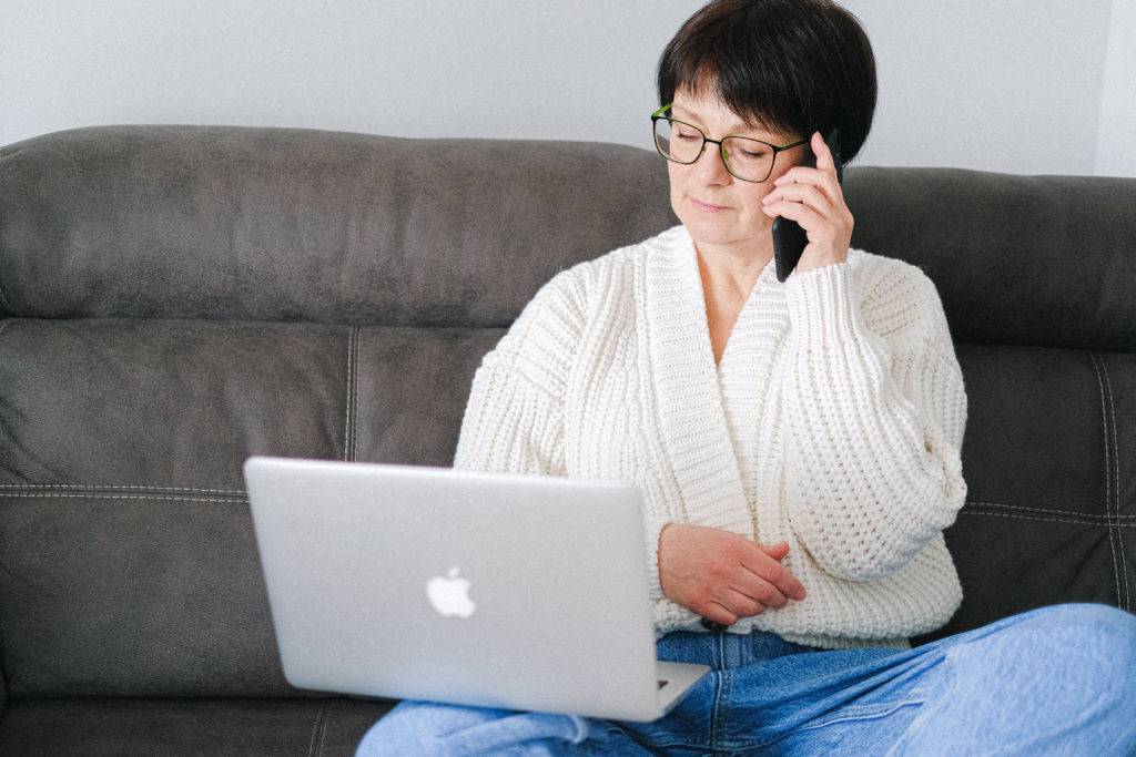 Woman on couch using cell phone and laptop