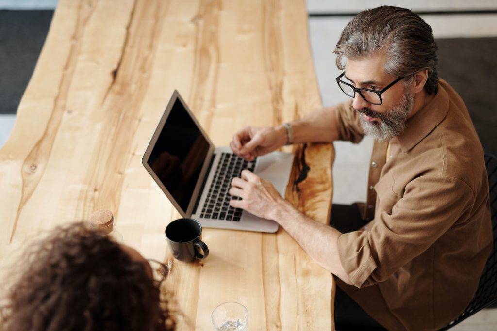 Man at table using laptop, looking woman at table