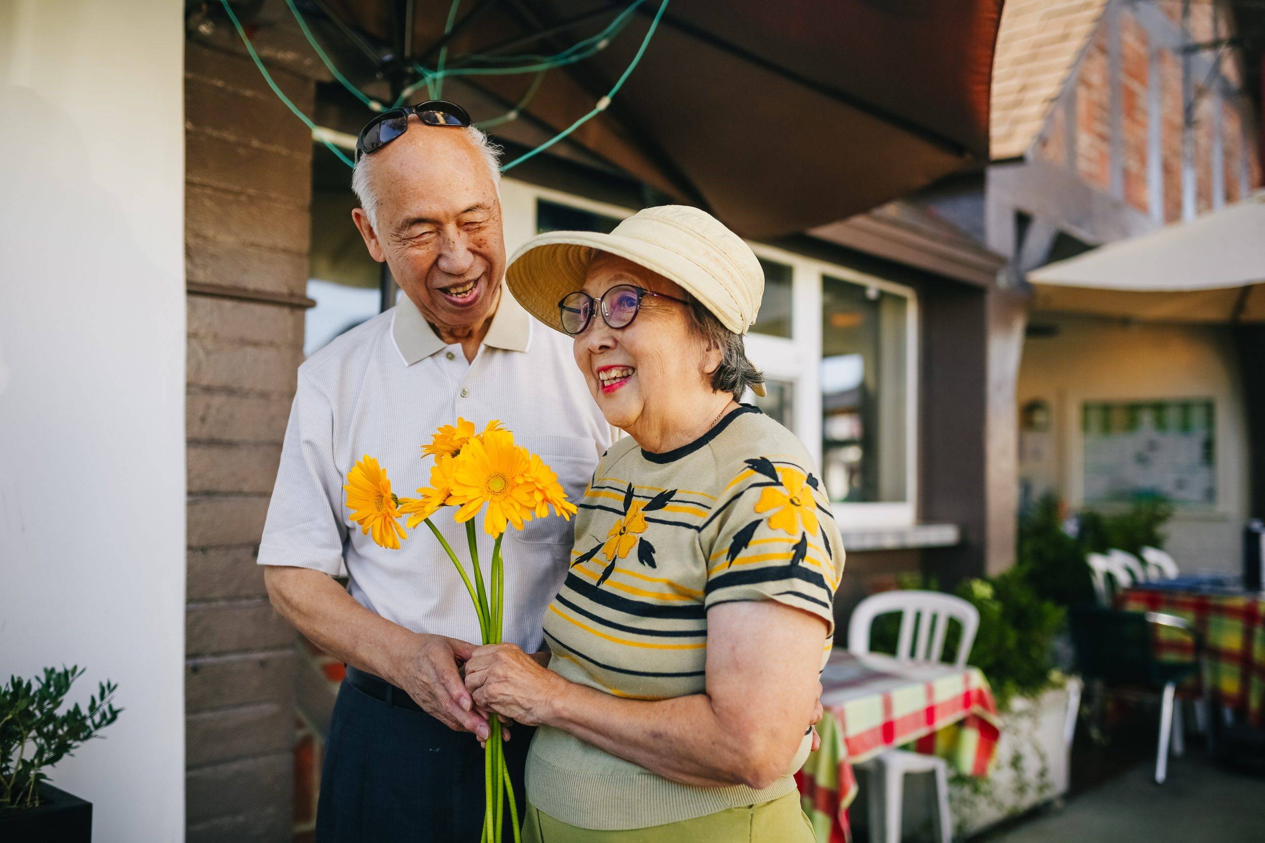 elderly man and woman outside with flowers, smiling