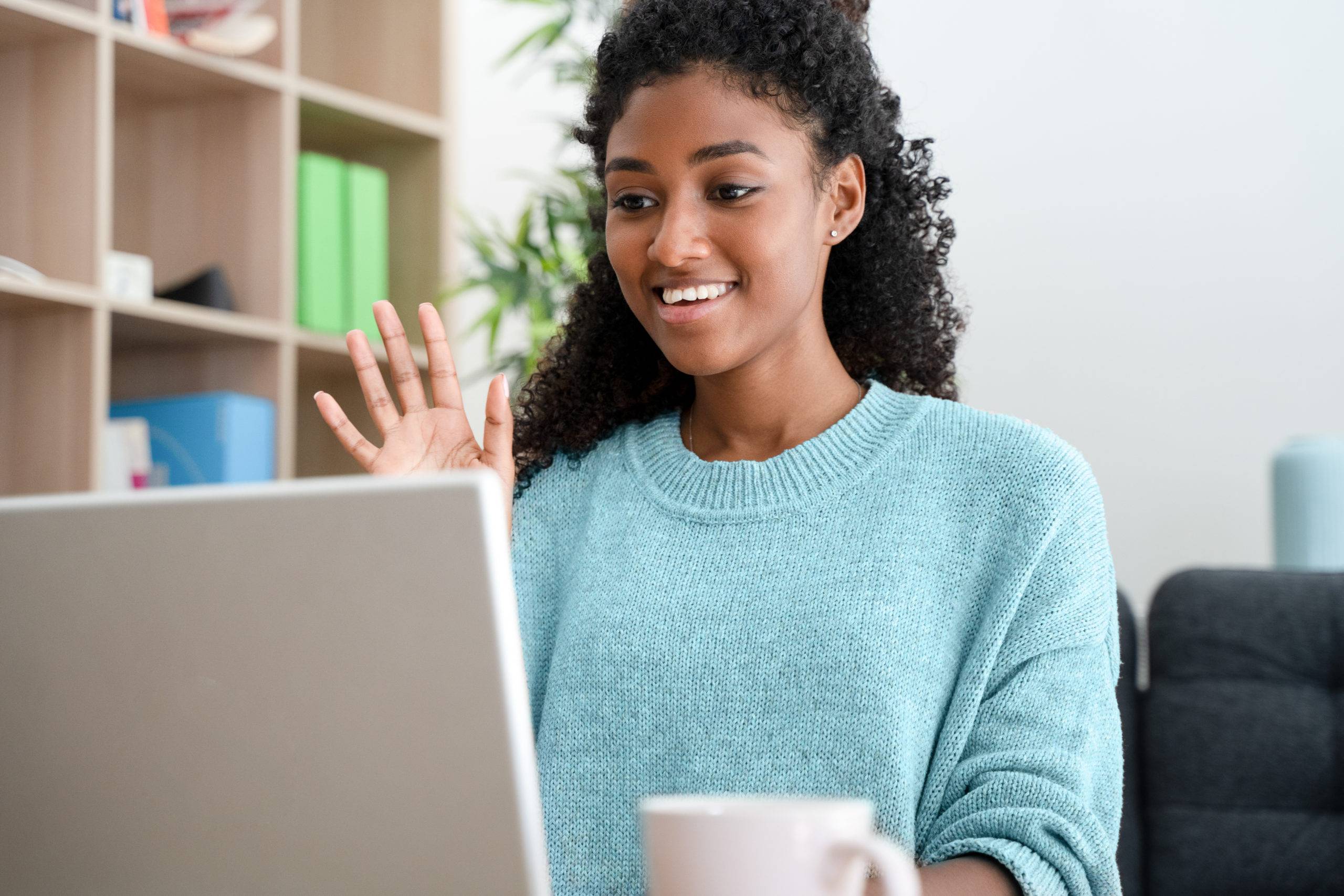 cheerful young woman smiling and waving on video call at home