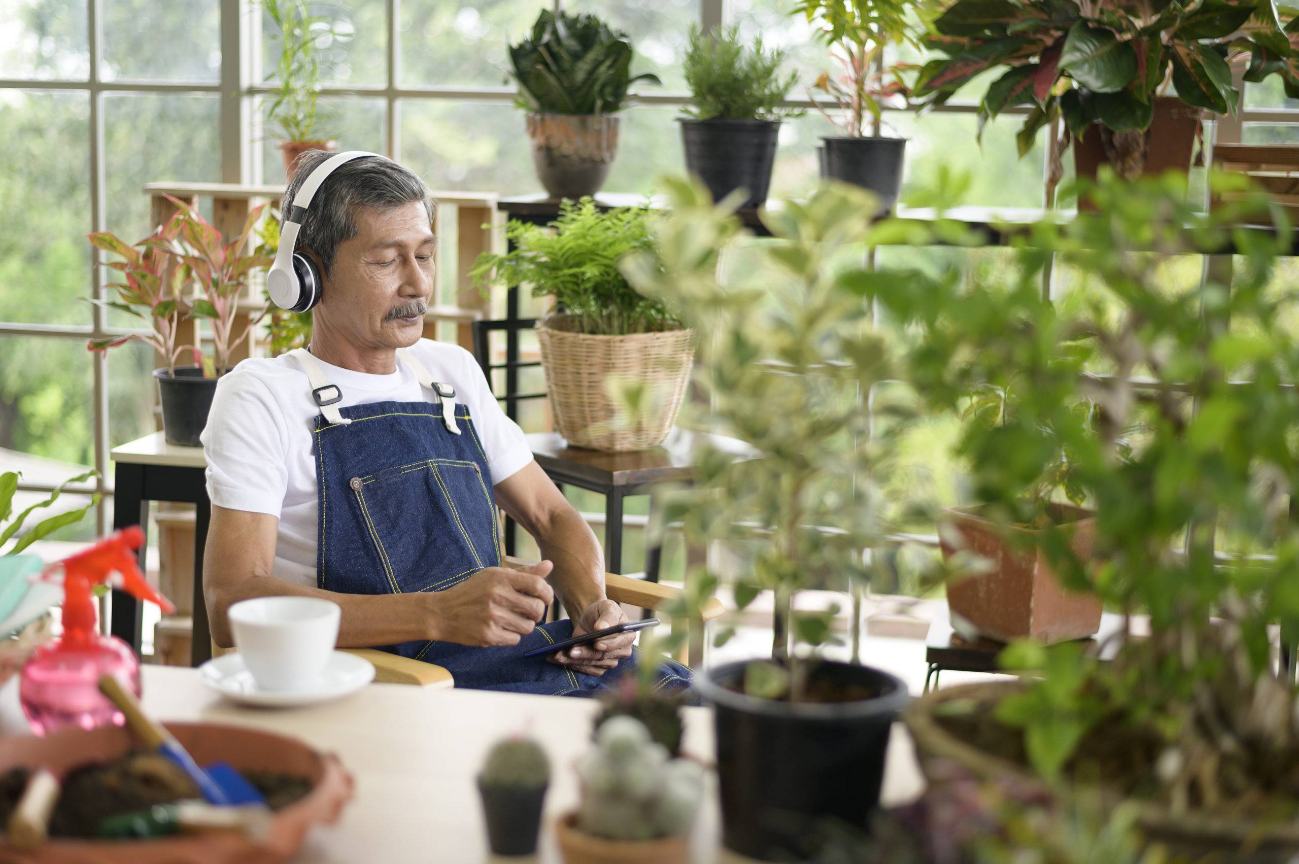 Elderly man with headphones sitting in garden with eyes closed