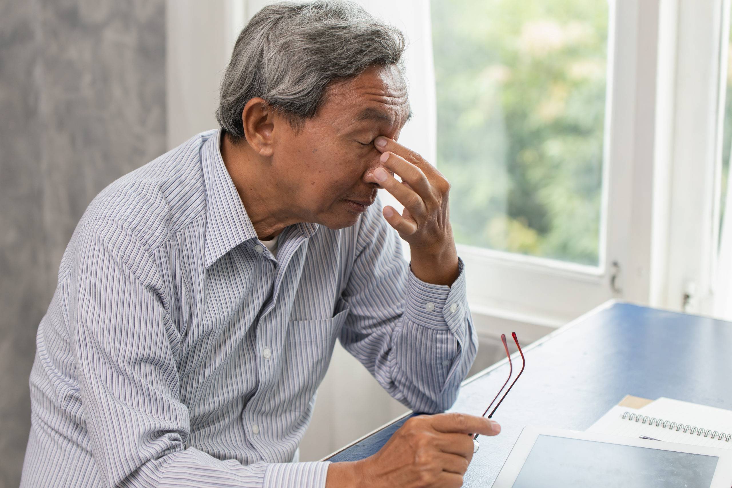Elderly man holds bridge of nose, signifying stress or tiredness
