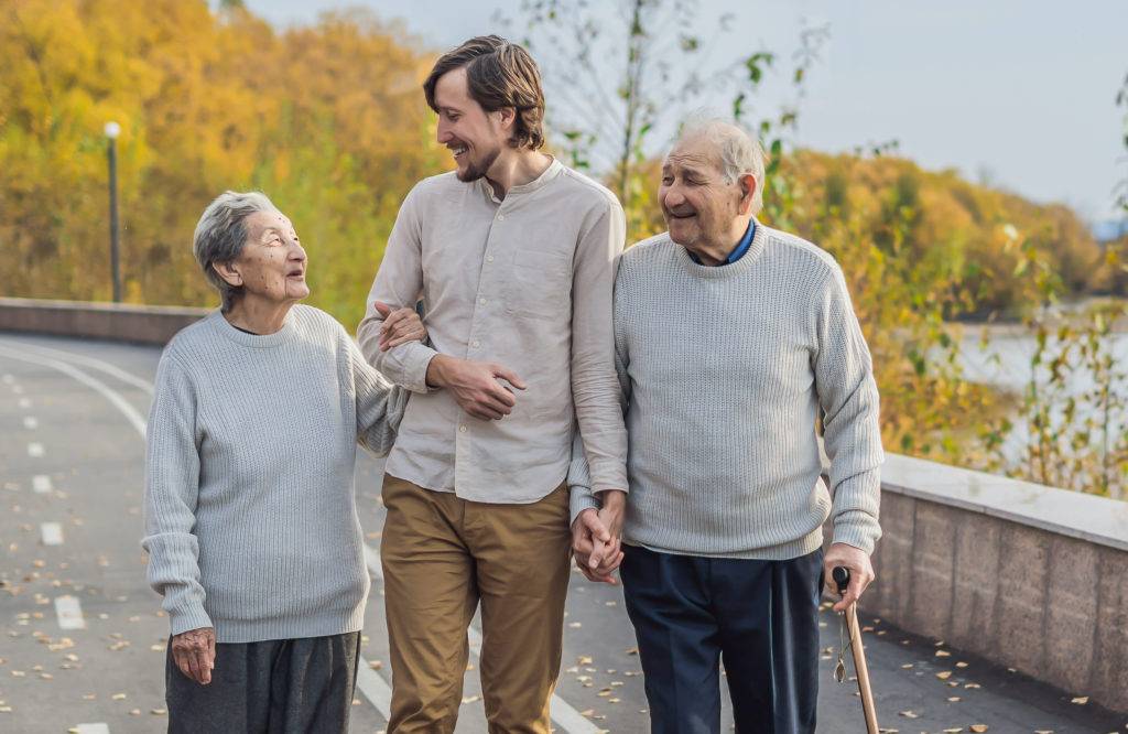 Elderly couple walks with young adult man thorugh park