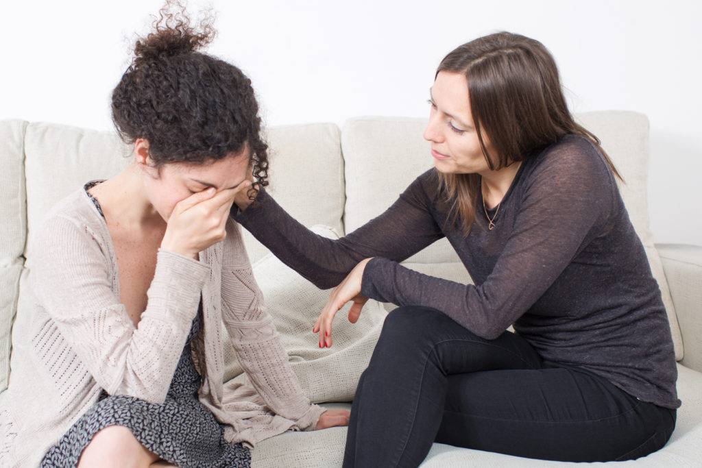 Two woman sitting on couch, one in distress and the other is providing comfort