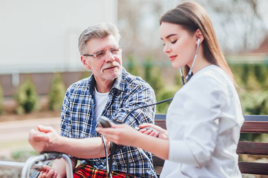 Nurse measures blood pressure of adult male, outside on bench