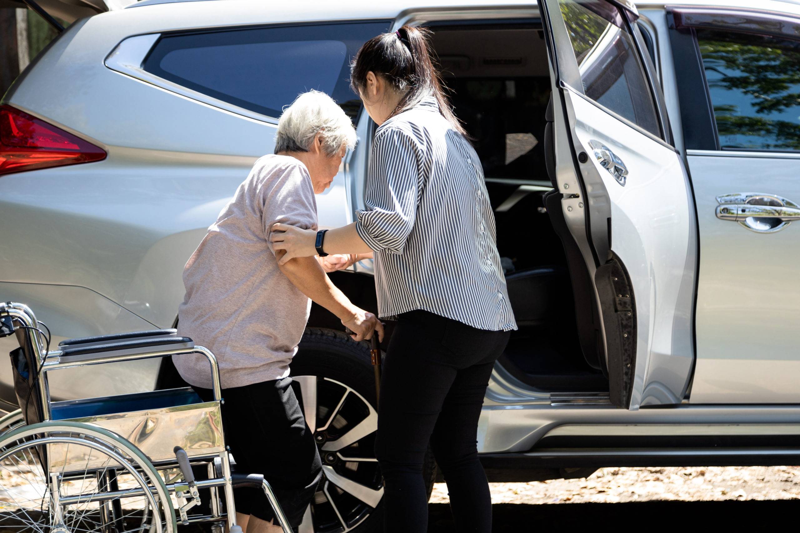 Elderly woman gets out of wheelchair and into car with support of adult daughter