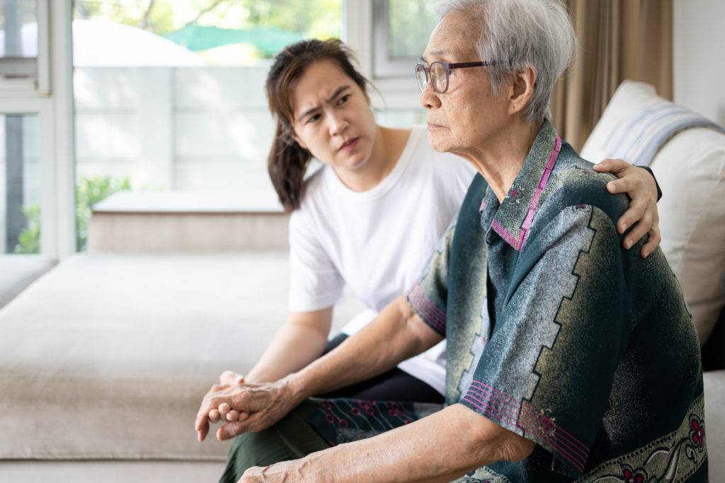 Elderly man and adult daughter, sitting on couch with serious faces
