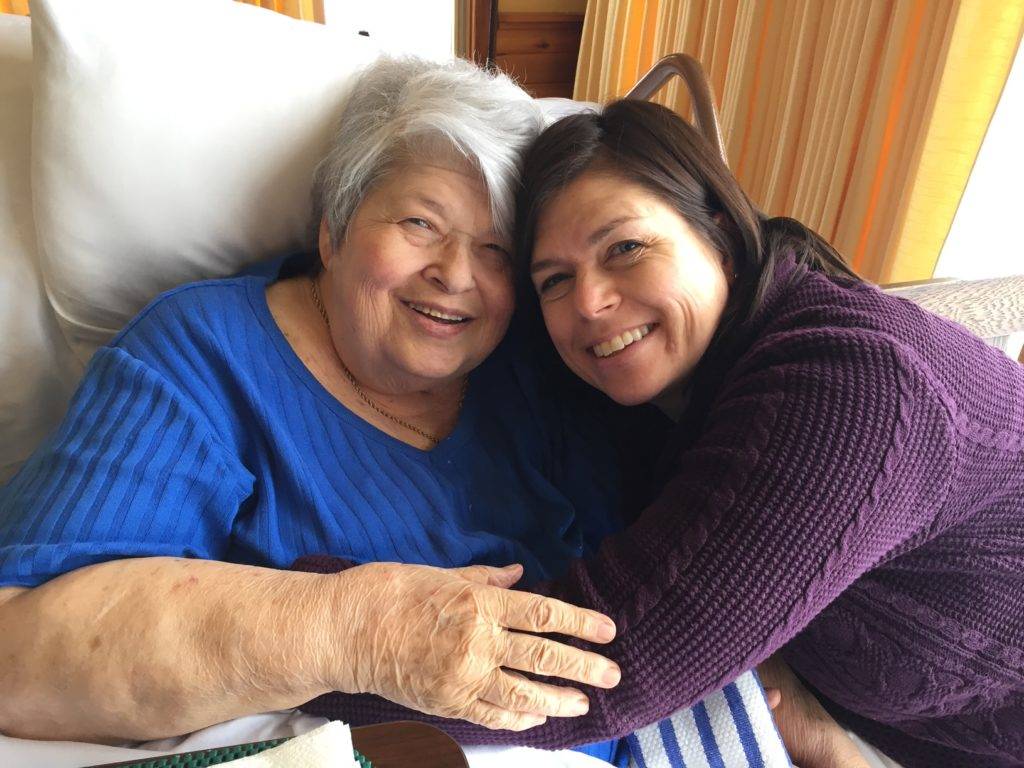Elderly woman in hospital bed, hugged by adult daughter