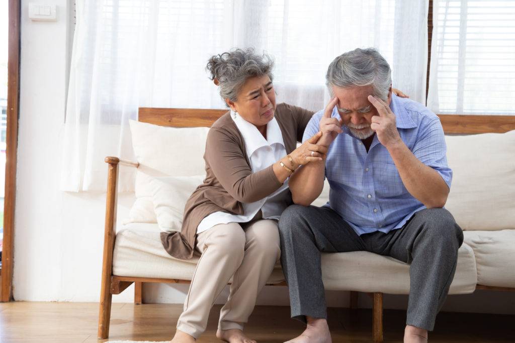 Elderly man and woman sitting on couch in distress