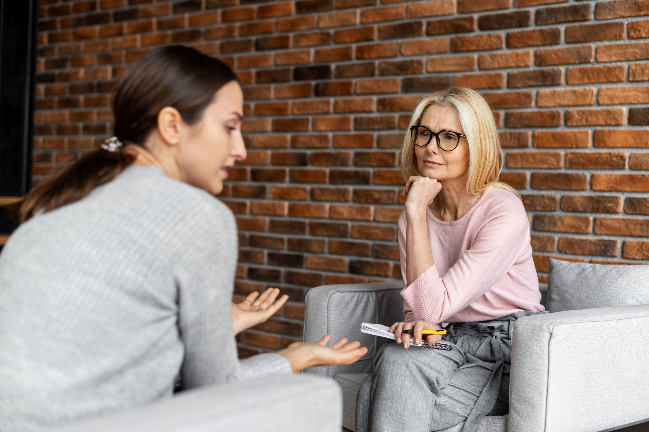 Female therapist seated, listens to female patient