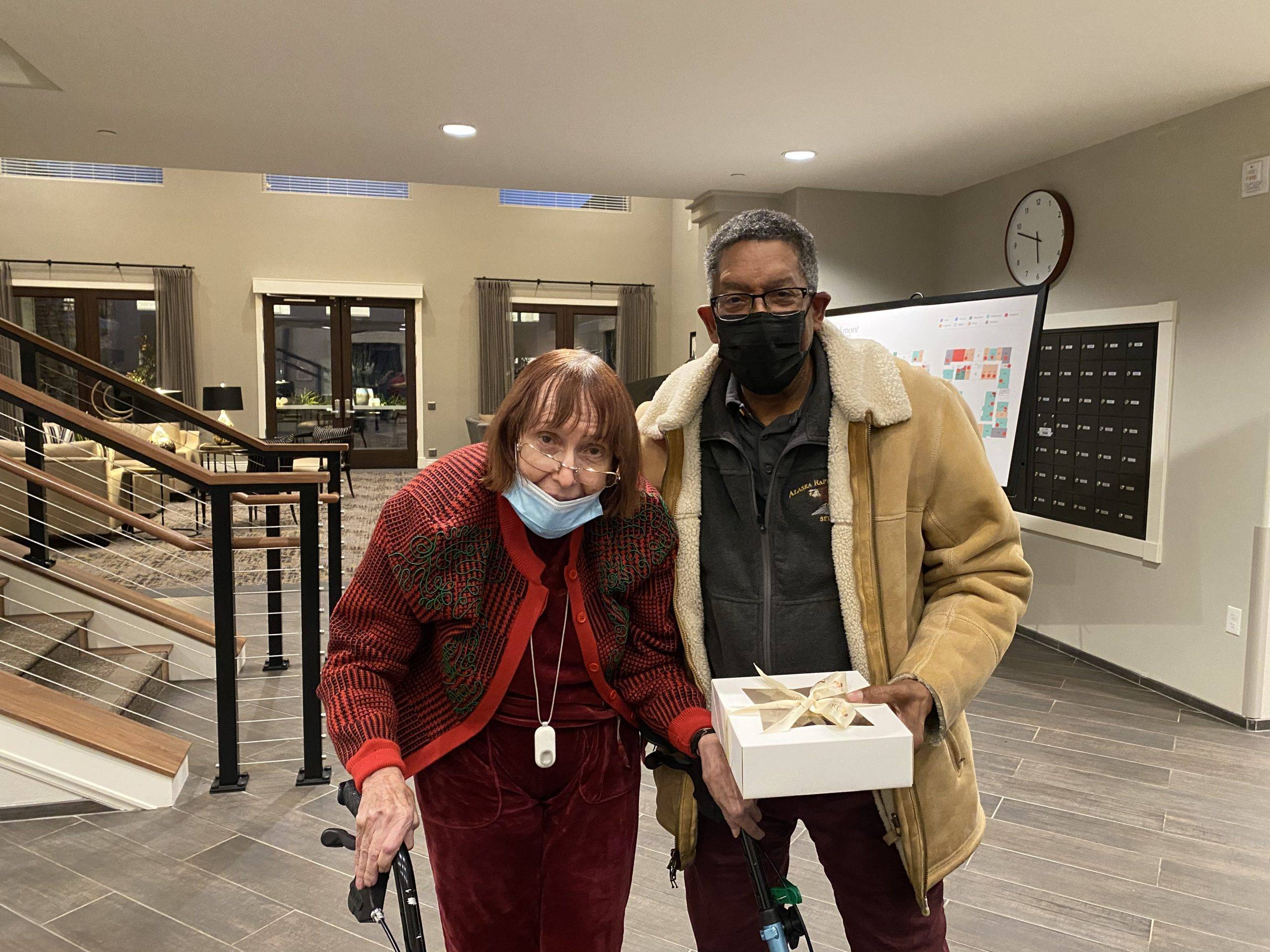 Adult man with elderly woman in public space, holding gift box