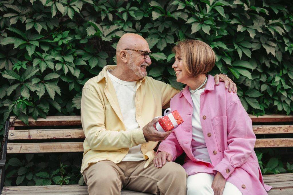 Elderly couple seated on bench outside with gift box
