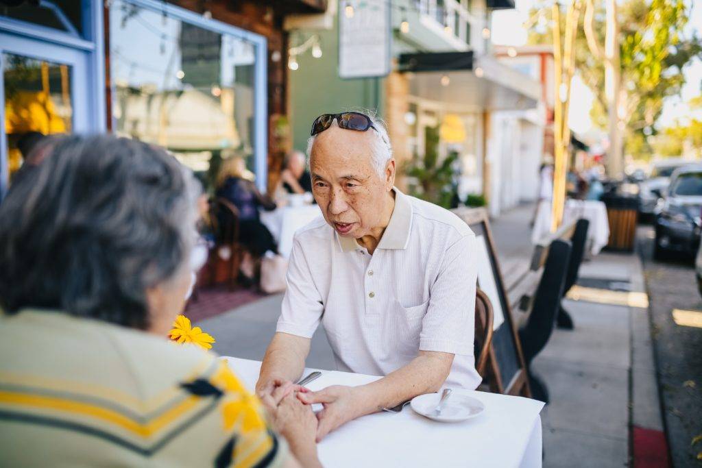 Elderly couple seated outdoor at restaurant, holding hands
