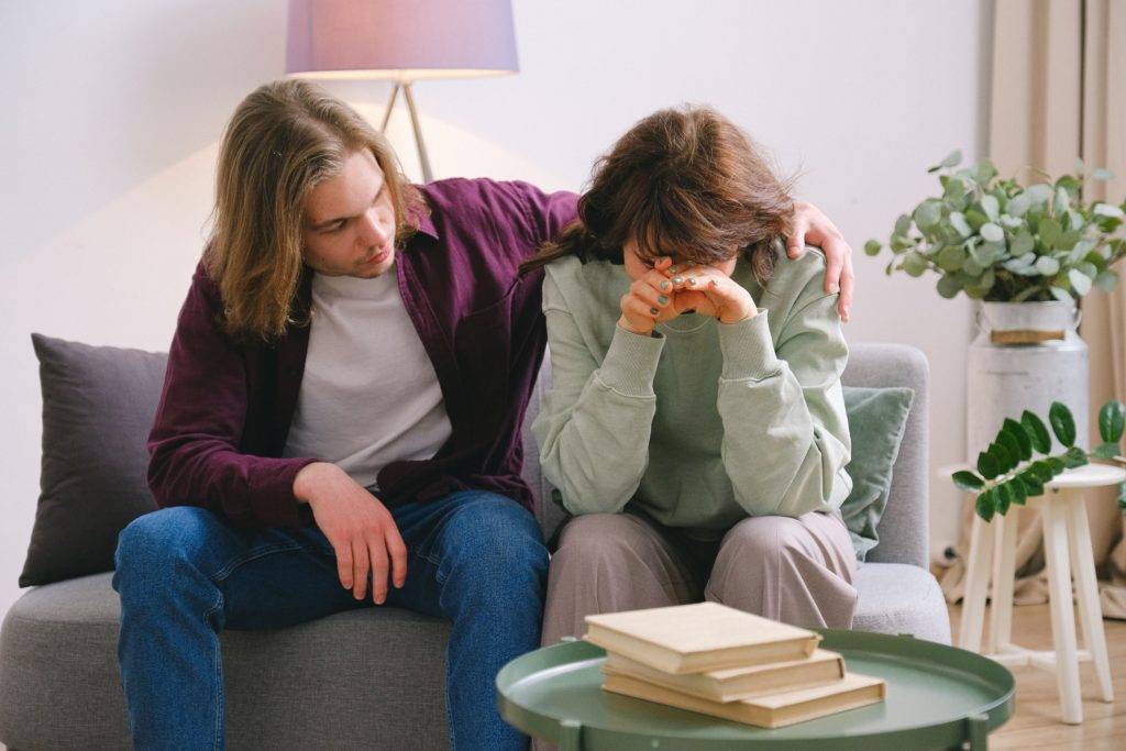 Adult woman sitting on couch in distress, adult man consoling her