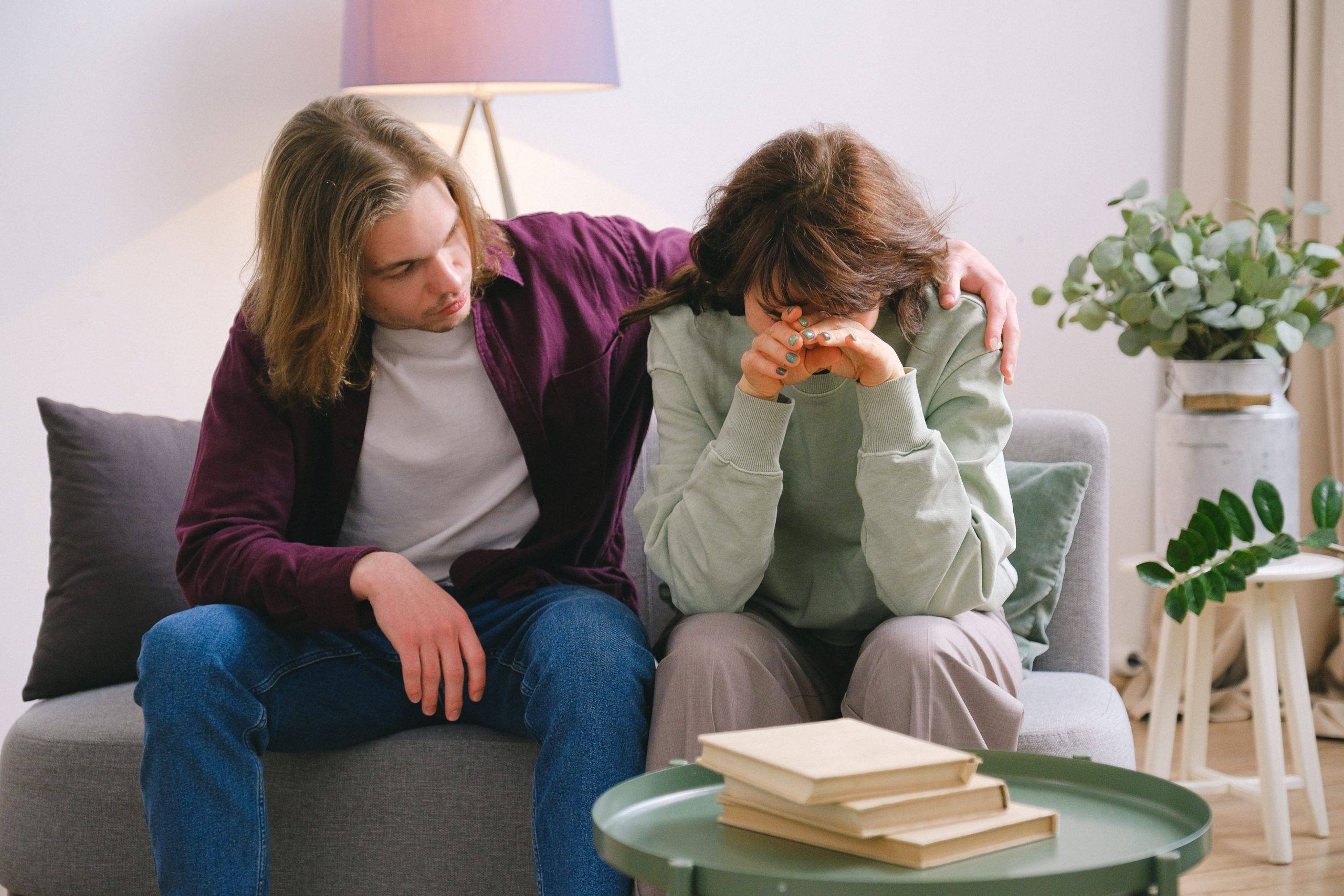 Adult woman sitting on couch in distress, adult man consoling her