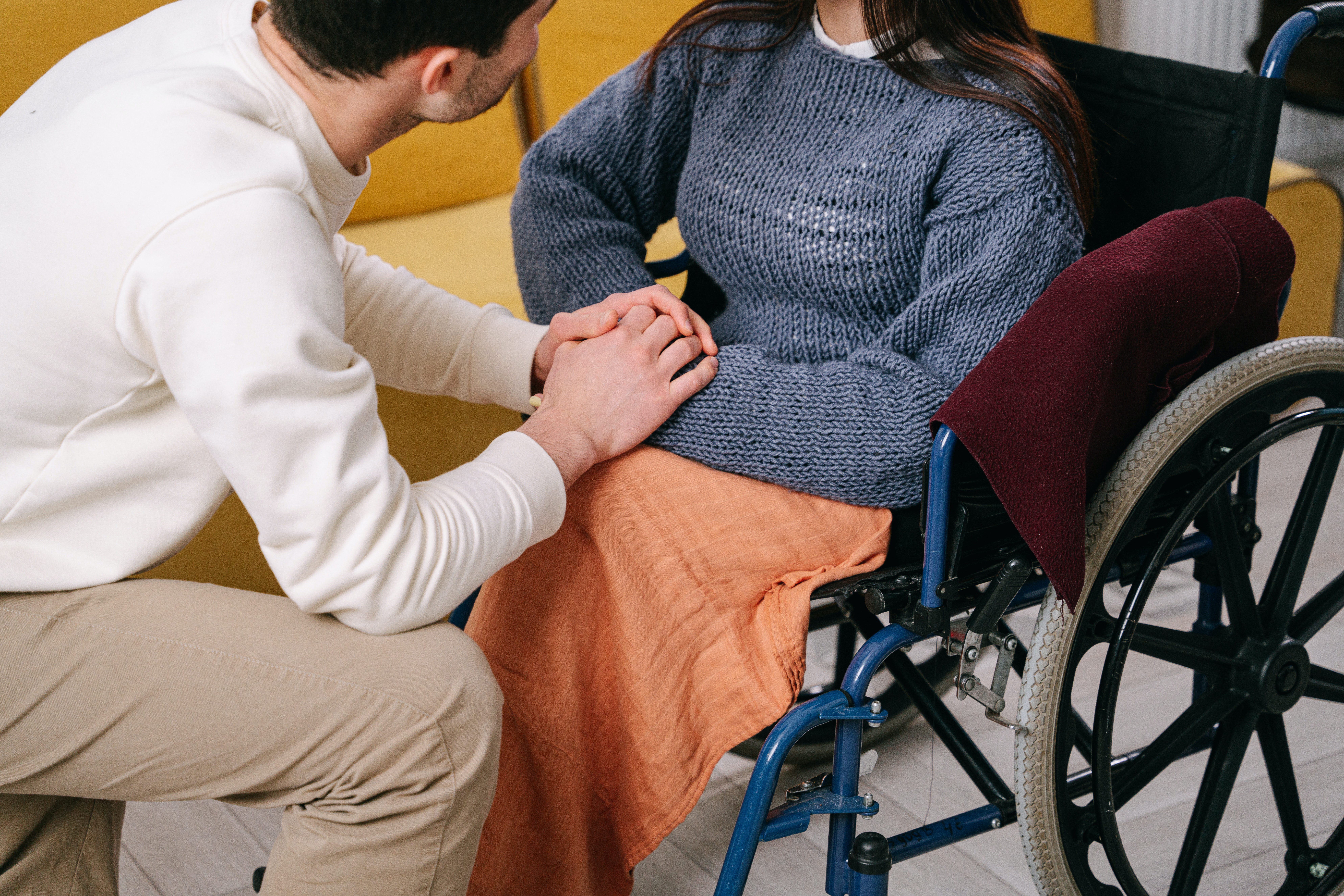 Young woman in wheelchair, young man holds hands next to her