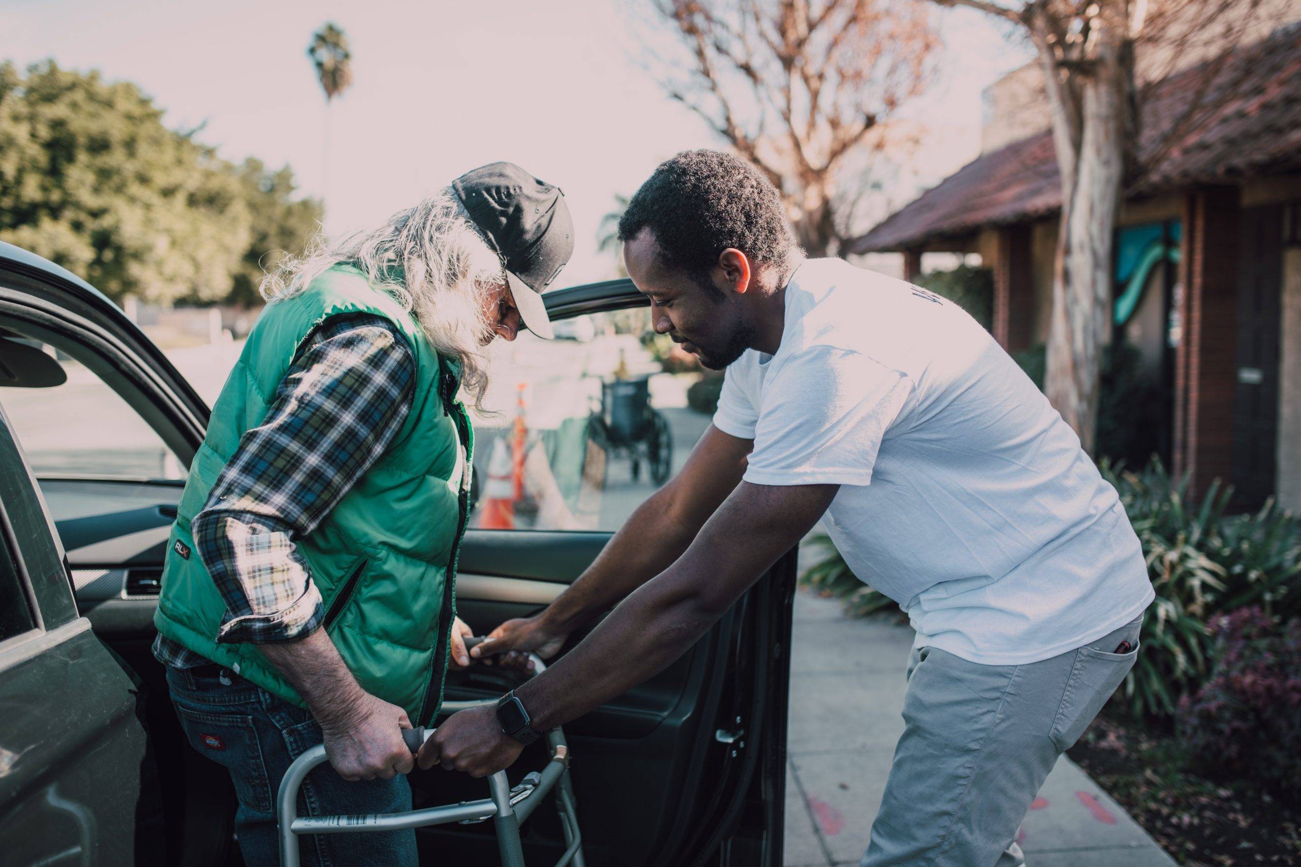 Adult man assists elderly woman with walker getting out of car