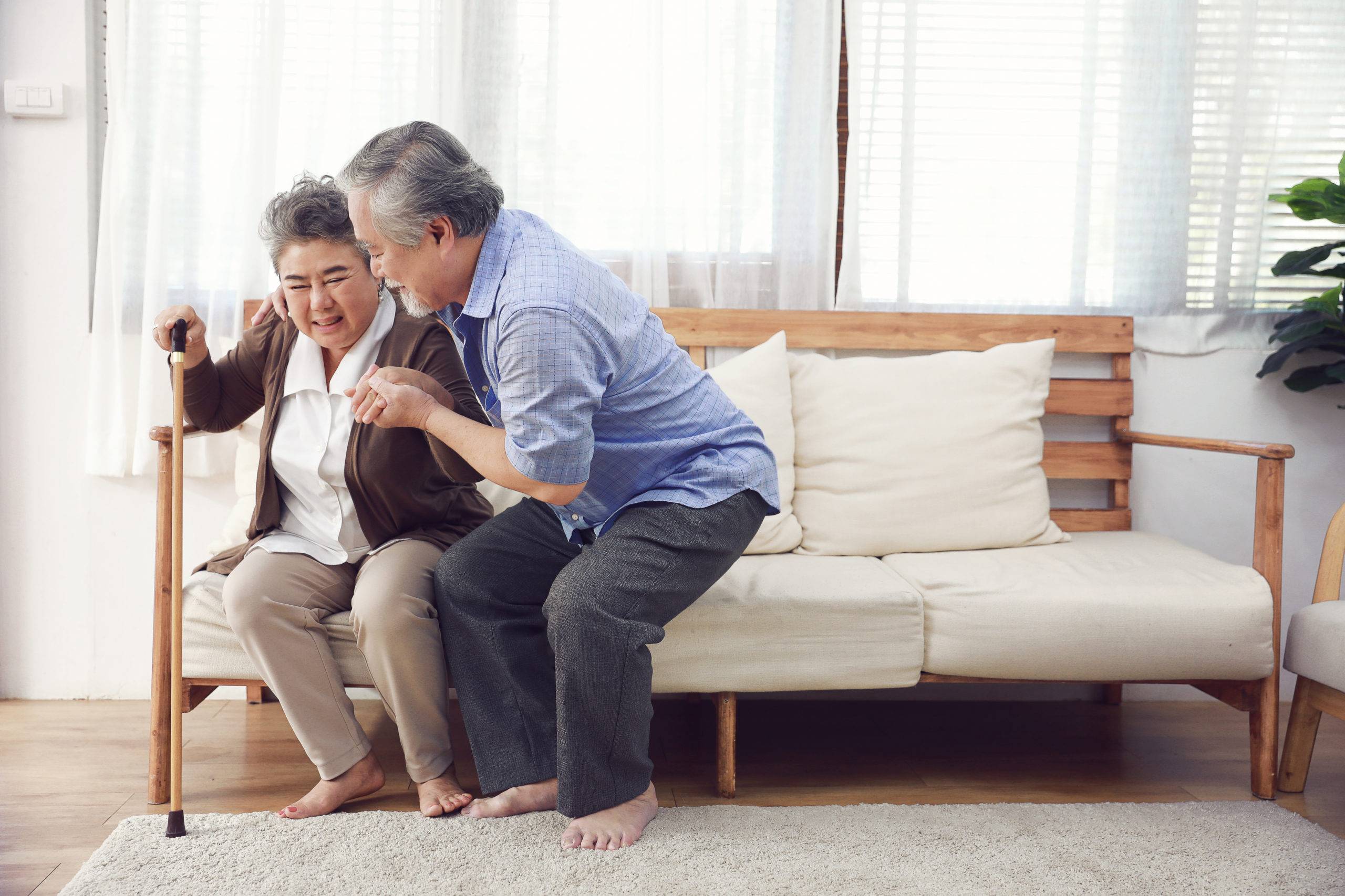 Elderly couple standing up from couch, woman using cane