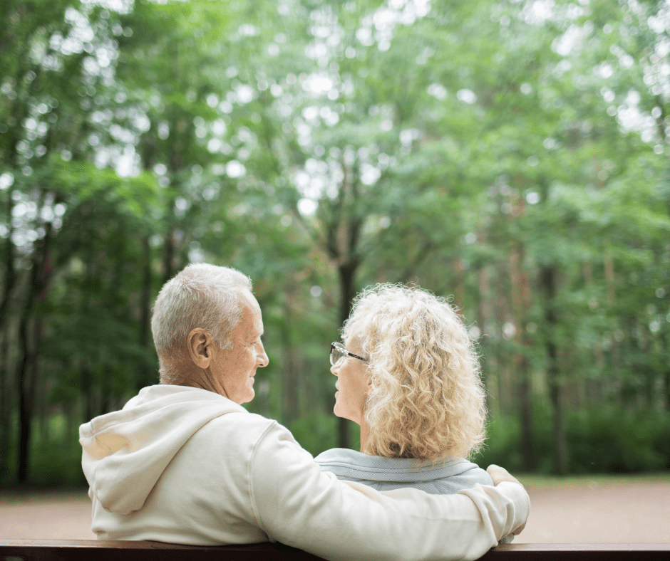 image shows two adults sitting on a park bench gazing at each other. the image is shot from behind them