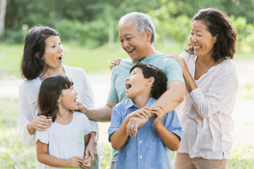 a multigenerational asian family standing outdoors and laughing while embracing