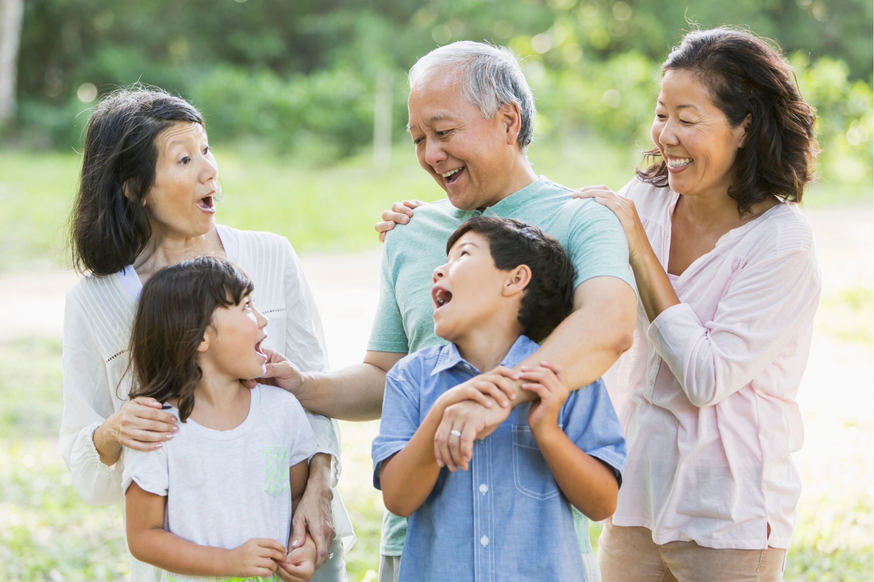 a multigenerational asian family standing outdoors and laughing while embracing