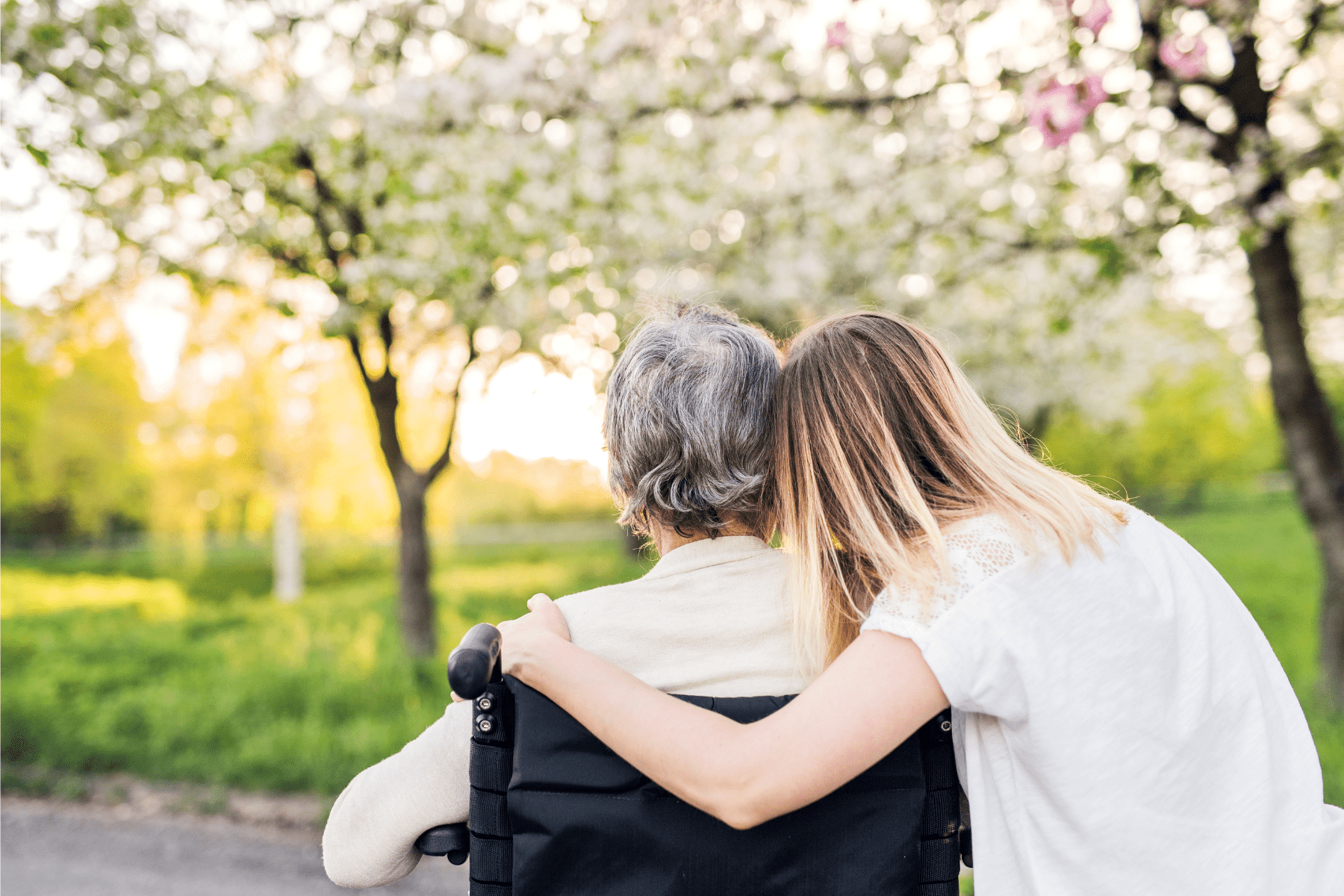 a blonde haired woman hugging an older woman in a wheelchair.